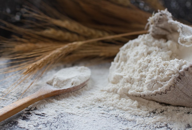 Harina de trigo en bolsa de arpillera con cuchara de madera y espigas de trigo