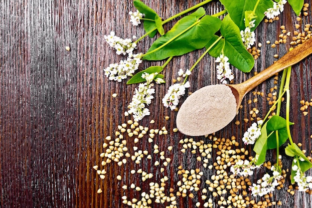 Harina de trigo sarraceno de cereales marrones en una cuchara de flores y hojas en el fondo de una tabla de madera desde arriba