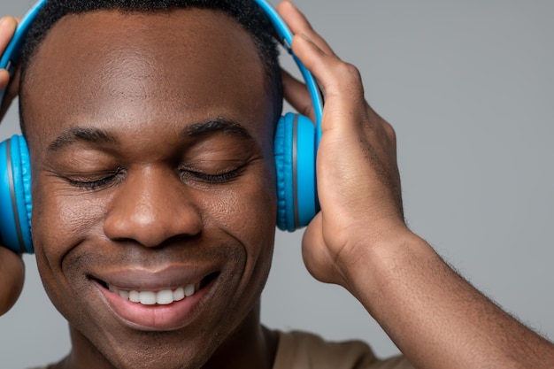 Harmonia. jovem afro-americano sorridente e satisfeito com os olhos fechados, usando fones de ouvido e tocando as mãos na cabeça