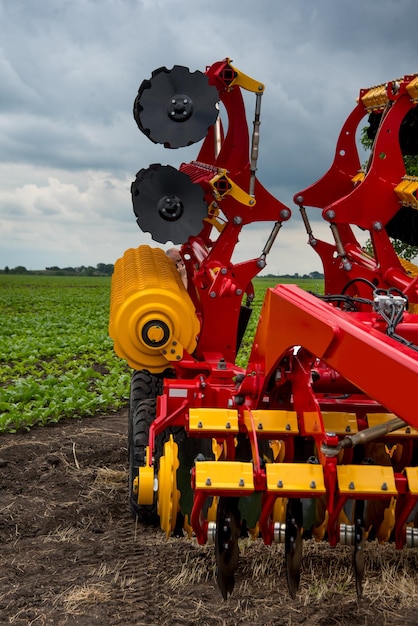 Foto harrowcultivator rojo y amarillo de pie plegado para el transporte cerca de un campo