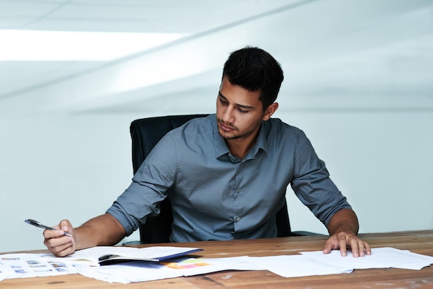 Hart arbeiten, um die Fristen einzuhalten Schnappschuss eines hübschen jungen Geschäftsmanns, der Papierkram erledigt, während er in einem modernen Büro arbeitet