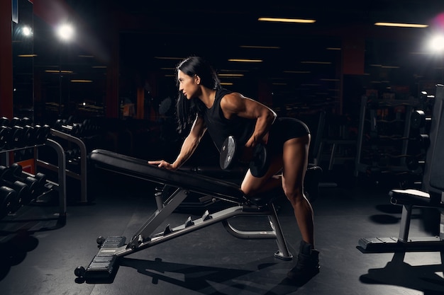 Hart arbeitende, fitte Frau, die Gewichte auf einer Schrägbank hebt, während sie im Fitnessstudio trainiert