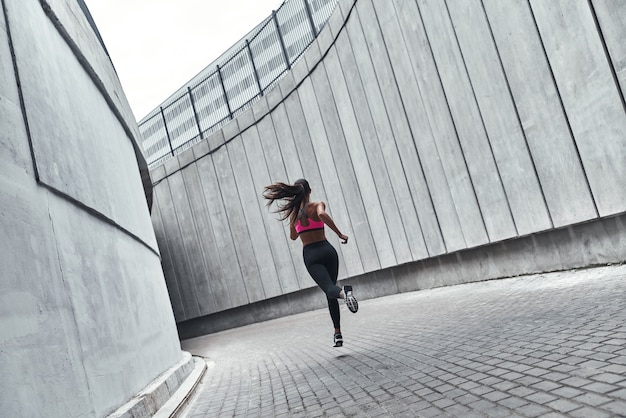 Hart drängen. Rückansicht in voller Länge der jungen Frau in Sportkleidung beim Joggen im Freien