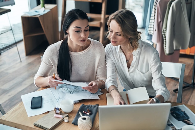 Harte Arbeitstage. Draufsicht auf schöne junge Frauen, die zusammenarbeiten, während sie in der Werkstatt sitzen