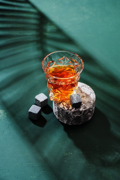Harte starke alkoholische Getränke im Glas: Cognac, Tequila, Scotch, Brandy oder Whisky auf grünem Hintergrund mit harten Lichtern und Schatten, Draufsicht.