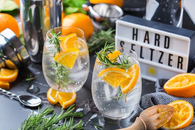 Harter Seltzer Cocktail mit Orange, Rosmarin und Eis auf einem Tisch. Sommer erfrischendes Getränk, Getränk auf einem schwarzen Tisch