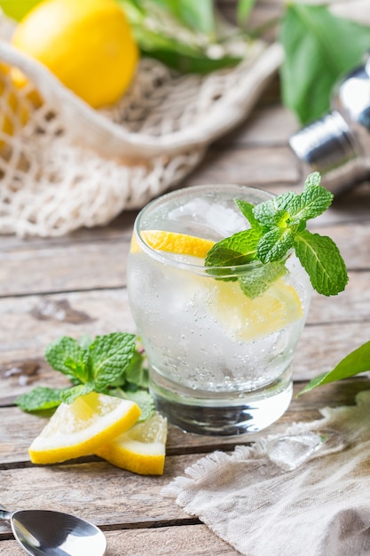 Harter Seltzer Cocktail mit Zitrone, Minze und Eis auf einem Tisch. Erfrischendes Sommergetränk, Getränk mit trendigem Accessoire ohne Abfall, Bambusstroh und Netzbeutel.