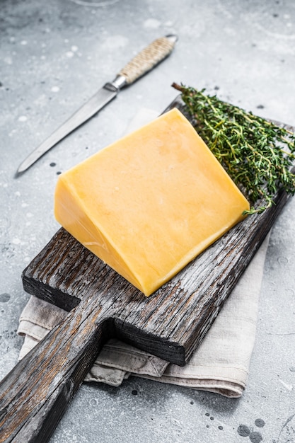 Hartkäse mit Messer auf Holzbrett. Parmesan. Grauer Hintergrund. Ansicht von oben.