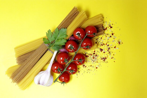 Hartweizenspaghetti und reife Kirschtomaten, Knoblauch und Gewürze. Frisches Grün. Hellgelber Hintergrund. Produkte zum Kochen leckerer Pasta.