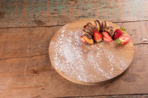 Foto haselnusscreme-croissant-dessert mit erdbeere auf holzbrett auf rustikalem tisch in der ecke in der bistro-draufsichtlandschaft