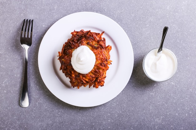 Hash brown y crema agria en un plato sobre un fondo de piedra gris