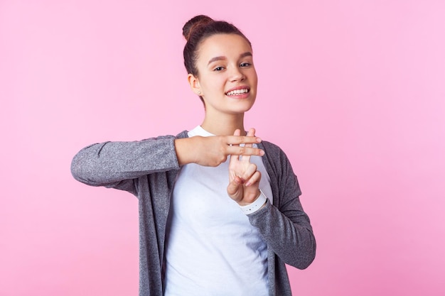 Hashtag popularidade na internet Retrato de adolescente alegre na moda com penteado de coque em roupas casuais, mostrando o símbolo de hash com os dedos sorrindo para a câmera studio shot isolado no fundo rosa