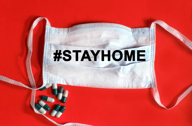 Hashtag stayhome - texto em uma máscara protetora, comprimidos em um fundo vermelho