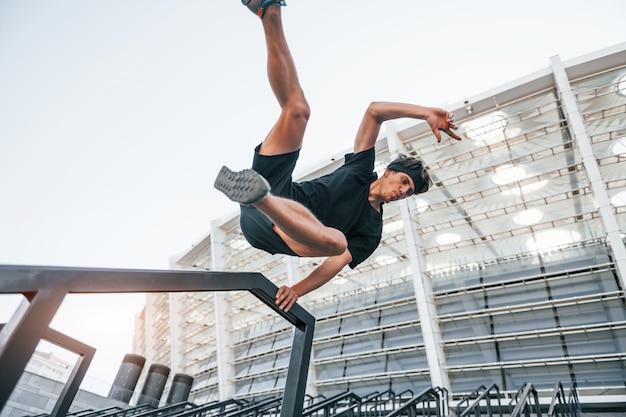 Hat parkour Junger Mann in sportlicher Kleidung trainiert tagsüber im Freien