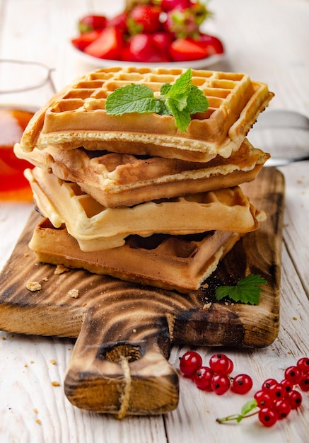 Haufen belgischer Waffeln auf geschnittenem Brett mit Erdbeeren und Sirup beiseite