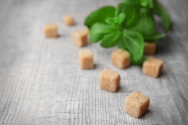 Haufen brauner Zuckerwürfel und Stevia auf grauem Holzhintergrund