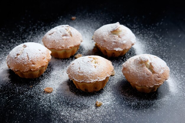 Haufen Cupcakes mit Zuckerpulver und Rosinen auf schwarzem Tisch