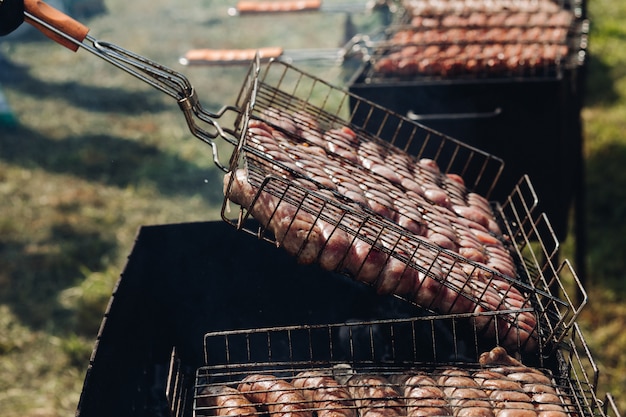 Haufen frischer appetitlicher Wurst, die auf Grill grillt, bereit für Picknick-Draufsicht im Freien