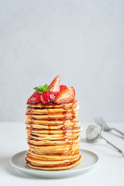 Haufen hausgemachter amerikanischer süßer Pfannkuchen, dekoriert mit Erdbeer-Minze-Blättern und Sirup-Topping