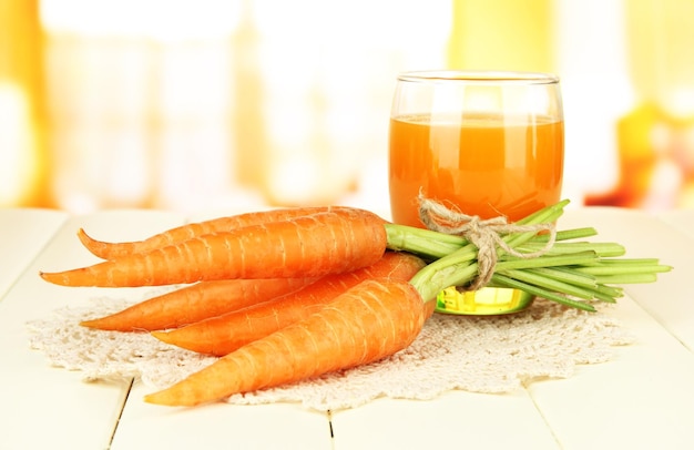 Haufen Karotten Glas Saft auf farbigem Holztisch auf hellem Hintergrund