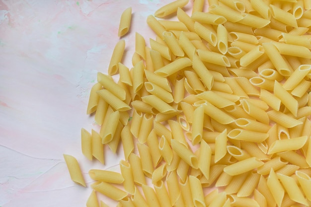 Haufen roher traditioneller italienischer Penne-Nudeln Rosa Hintergrund Nahaufnahme des Kopierbereichs