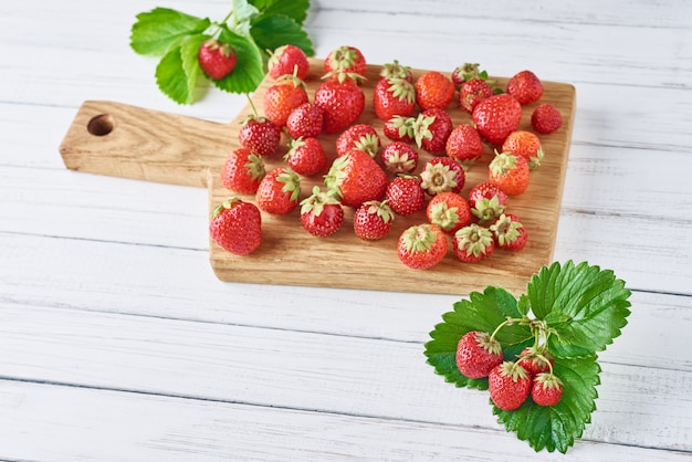 Haufen von frischen Erdbeeren mit Schneidebrett auf einem weißen hölzernen Hintergrund. Gesunde Ernährung