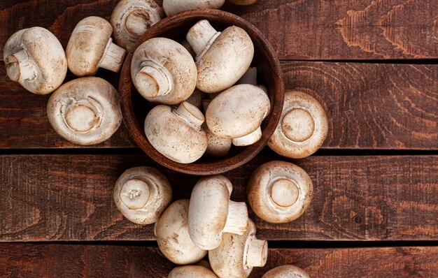 Haufen von Pilzen, Champignons in der Holzschale auf braunem Tisch, Draufsicht