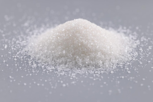 Haufen von Zuckerkristallen auf grauer Oberfläche, konzentrieren Sie sich auf Haufen von süßem Pulver, um es in Gerichte hinzuzufügen