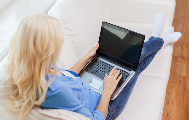 haus-, technologie- und internetkonzept - lächelnde frau mit laptop, die zu hause auf der couch sitzt