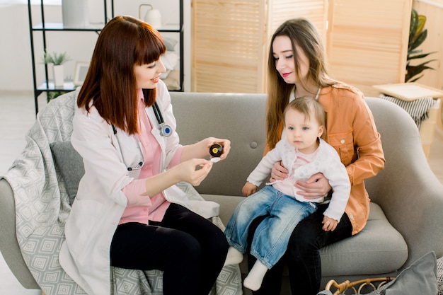 Hausärztin im weißen Kittel untersucht kleines Baby zu Hause oder in der Klinik. Freundliche Arzt Therapeut Aussehen gibt Hustensaft