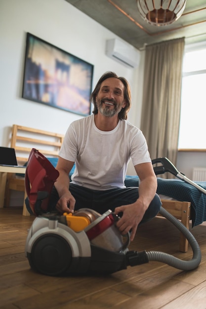 Hausarbeit. Mann sitzt auf dem Boden und sammelt den Staubsauger