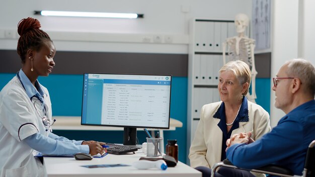 Foto hausarzt berät mann mit körperlicher behinderung, spricht mit patient und frau beim chekcup-besuch. rollstuhlfahrer mit beeinträchtigung bei der gesundheitsuntersuchung im medizinischen kabinett.