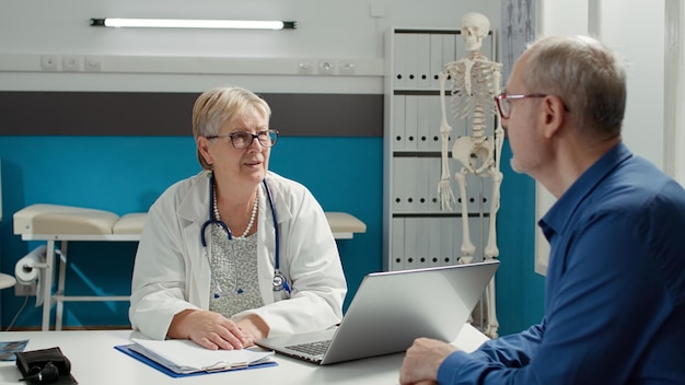 Hausarzt im Gespräch mit pensioniertem Patienten bei Kontrolltermin. Arzt konsultiert alten Mann mit Krankheit in Arztpraxis und gibt Behandlung, um bei der Genesung zu helfen.