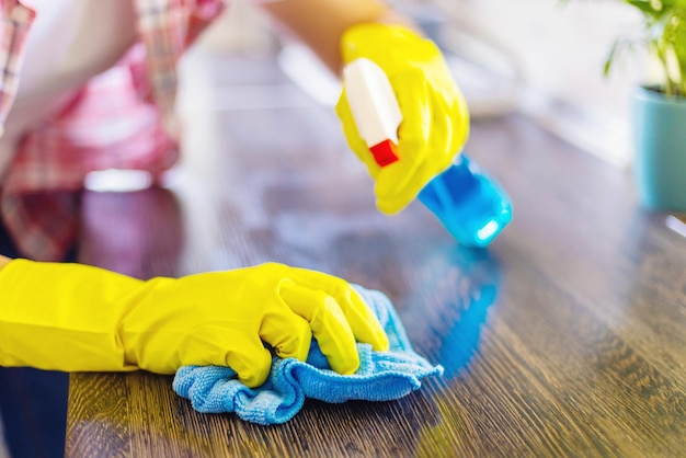 Hausfrau in gelben Handschuhen wischt Staub mit Spray-Reinigungsmittel und Tuch