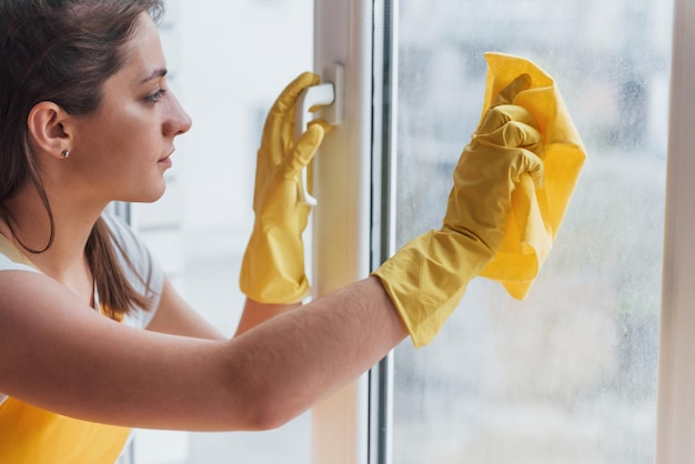 Hausfrau in gelber Uniform, die Fenster putzt Konzeption der Hausrenovierung