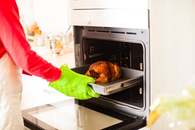 Hausfrau in Schürze kocht ganzes gegrilltes Hähnchen. Weihnachtsabend, Familientreffen