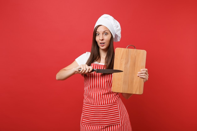 Hausfrau Köchin oder Bäckerin in gestreifter Schürze, weißes T-Shirt, Haubenköche isoliert auf rotem Wandhintergrund. Haushälterin Frau mit Holzschneidebrett, Messer. Mock-up-Kopierraumkonzept.