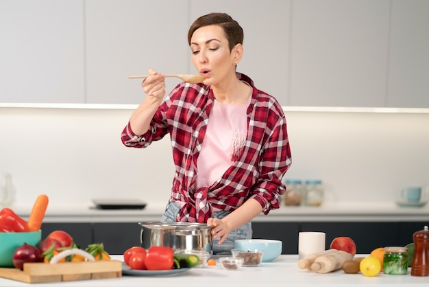 Hausfrau mit einer kurzen Frisur, die ein Essen probiert, während sie das Mittagessen für die Familie in der Moderne kocht