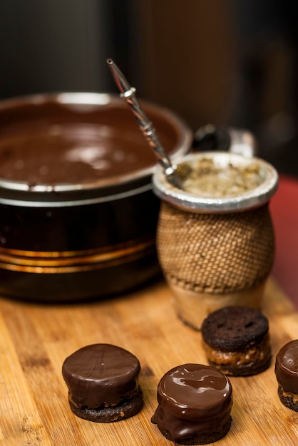 Hausgemachte argentinische Alfajores in Schokolade getaucht auf einem Holzbrett neben Yerba Mate Tee und der Kanne mit der Schokolade. Konzept der regionalen, traditionellen Küche.