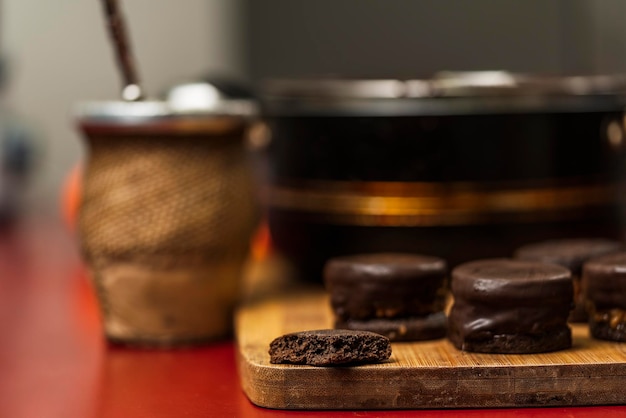 Hausgemachte argentinische Alfajores in Schokolade getaucht auf einem Holzbrett neben Yerba Mate Tee und der Kanne mit der Schokolade