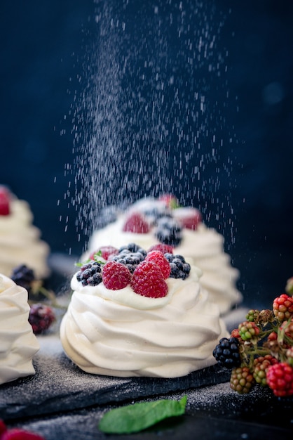 Hausgemachte Baiser-Basis für Kuchen Pavlova mit frischen Blaubeeren und BlackBerry und Puderzucker auf schwarzem Beton