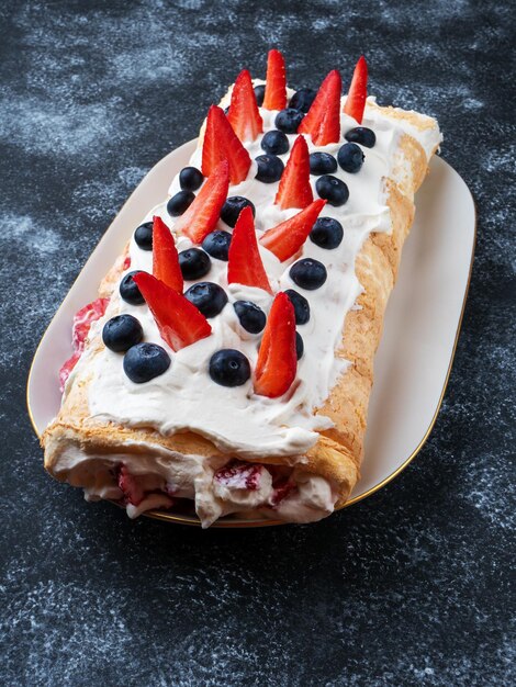 Hausgemachte Baiserroulade Baiserrollenkuchen Pavlova mit Sahneerdbeeren und Heidelbeeren Seitenansicht