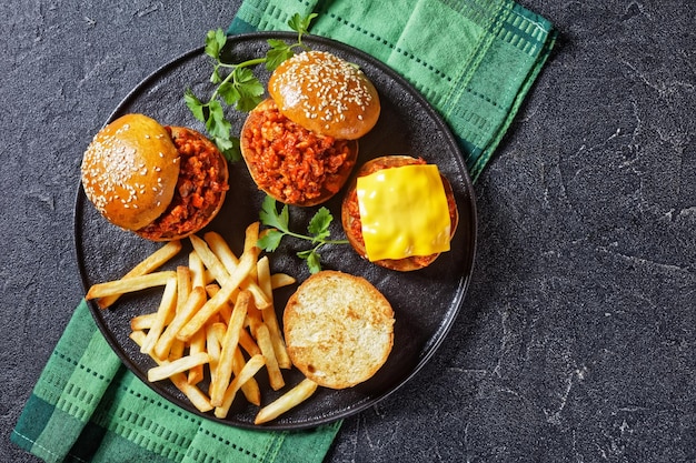 hausgemachte BBQ Sloppy Joe Sandwiches mit Pommes Frites auf einem schwarzen Teller, flach gelegt, freier Platz