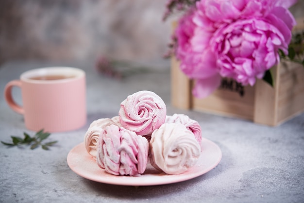 Hausgemachte Beeren Marshmallow in einem Teller ist auf dem Tisch mit einer Tasse Tee. Puderzucker fällt auf Marshmallows.