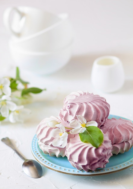 Hausgemachte Beeren-Marshmallows auf einem blauen Teller mit Apfelbaumblüten und Teetassen auf einem weißen Tisch