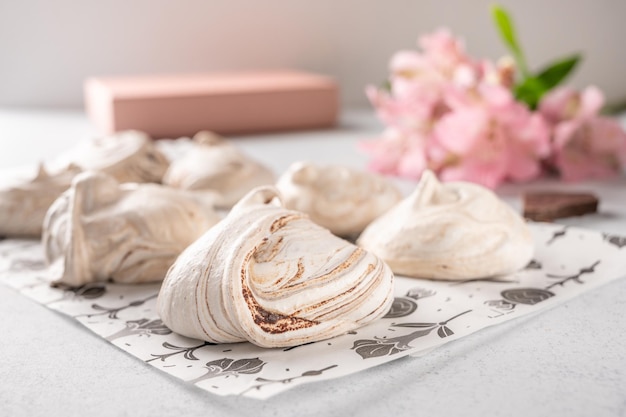 Hausgemachte beliebte Eier Dessert Baiser auf einem Backpapier auf hellem Hintergrund neben rosa Blume und