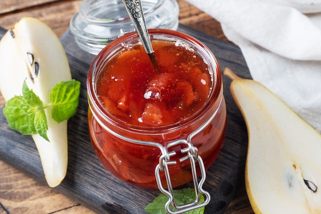 Hausgemachte Birnenmarmelade in einem Glas und frische Birnen auf einem hölzernen Hintergrund.