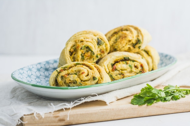 Hausgemachte Brötchen mit Knoblauch, grüner Petersilie und Paprika in einem Teller mit Serviette und Holzschneidebrett weiß.