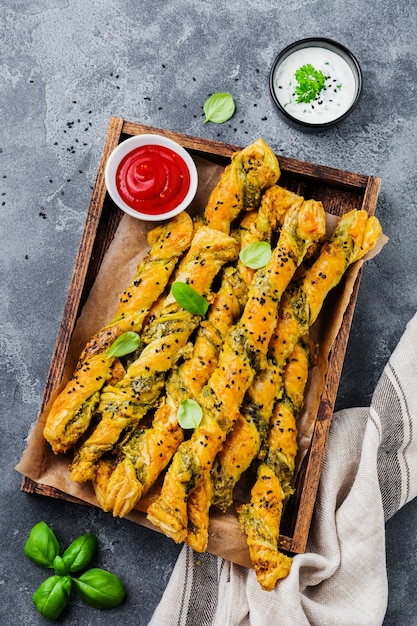 Hausgemachte Brotstangen mit Käse, Pesto-Sauce und schwarzen Sesamkörnern auf grauer Steinweinleseoberfläche