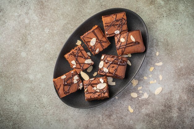 Hausgemachte Brownies mit Mandelblättern auf einem dunklen Teller auf einem hölzernen Hintergrund.